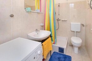 A bathroom with a white sink, a bathtub, a toilet, and a shower curtain. - Apartment Burica (Primosten)