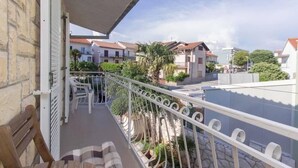 A balcony with a white railing, a wooden bench, and a view of neighboring houses and greenery. - Apartment Burica (Primosten)