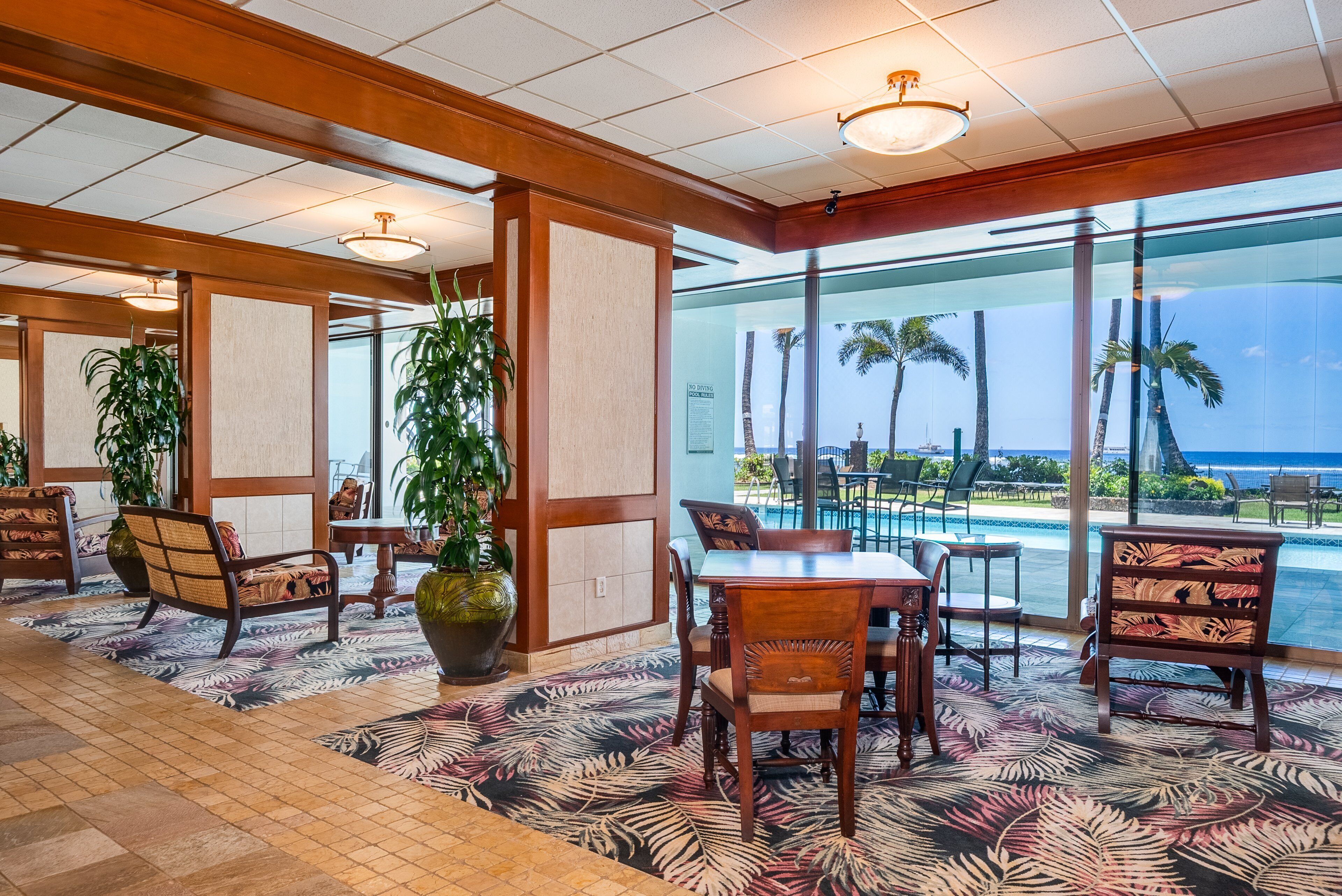 Vestíbulo de hotel con vista a una piscina, muebles de madera y decoración tropical.