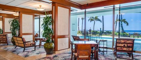 Vestíbulo de hotel con vista a una piscina, muebles de madera y decoración tropical.
