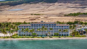 Et hotel med flere etager, udsigt til stranden og et bjergrigt landskab i baggrunden.