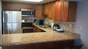 Una cocina con encimeras de granito, electrodomésticos de acero inoxidable, armarios de madera y salpicadero de azulejos.