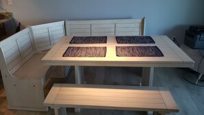 Un comedor con una mesa blanca y asientos tipo banco, una zona de cocina con mostrador y taburetes, e impresora en el suelo.