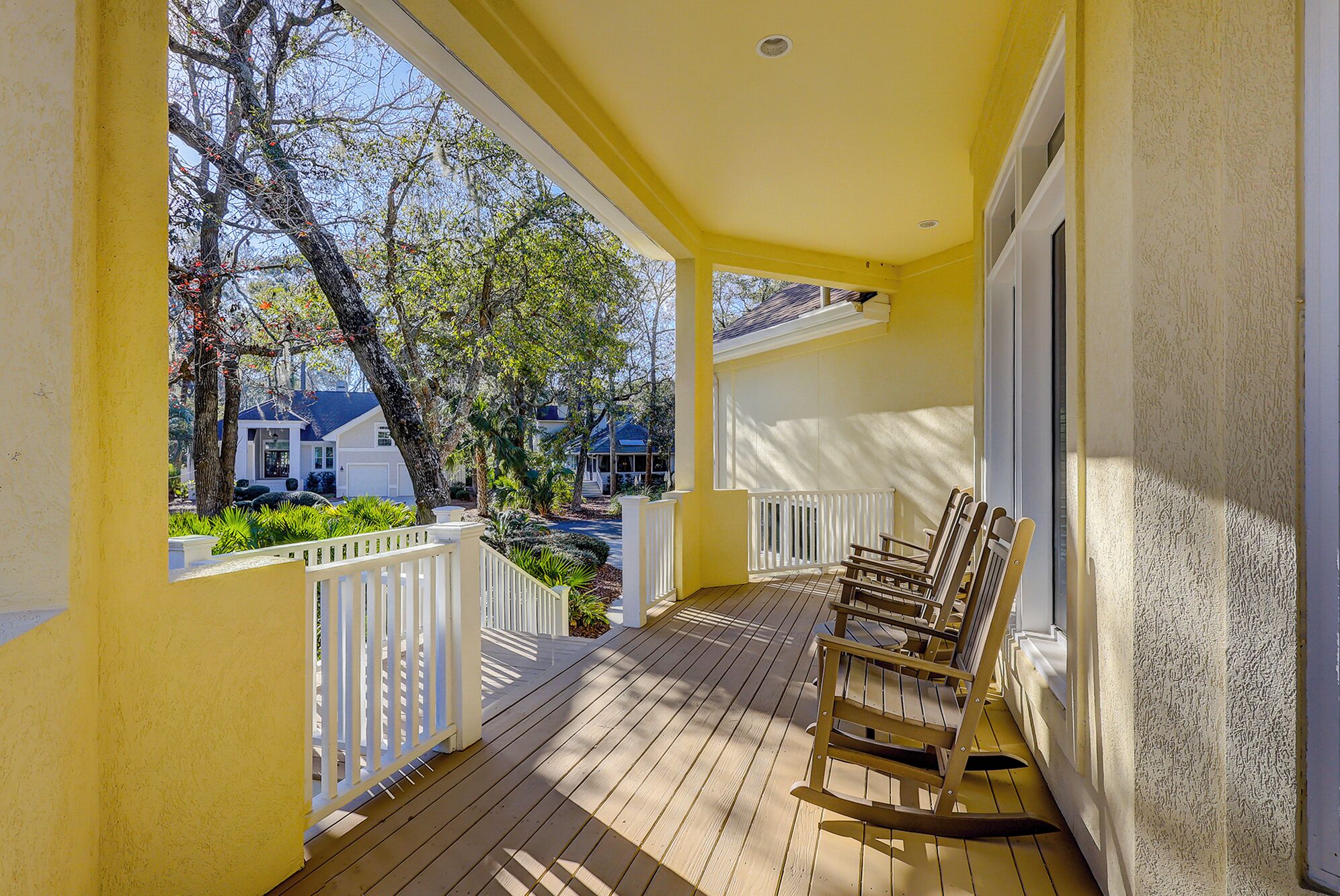 A wooden porch with a rocking chair, white railings, and a view of neighboring houses and trees.