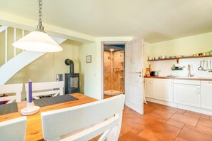 A kitchen with white cabinets, a wooden table, a hanging light fixture, and a shower area visible through an open door.
