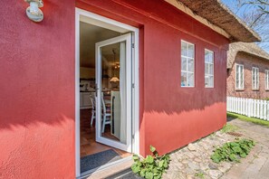 A red building with a white door, a thatched roof, and a white fence in the background.