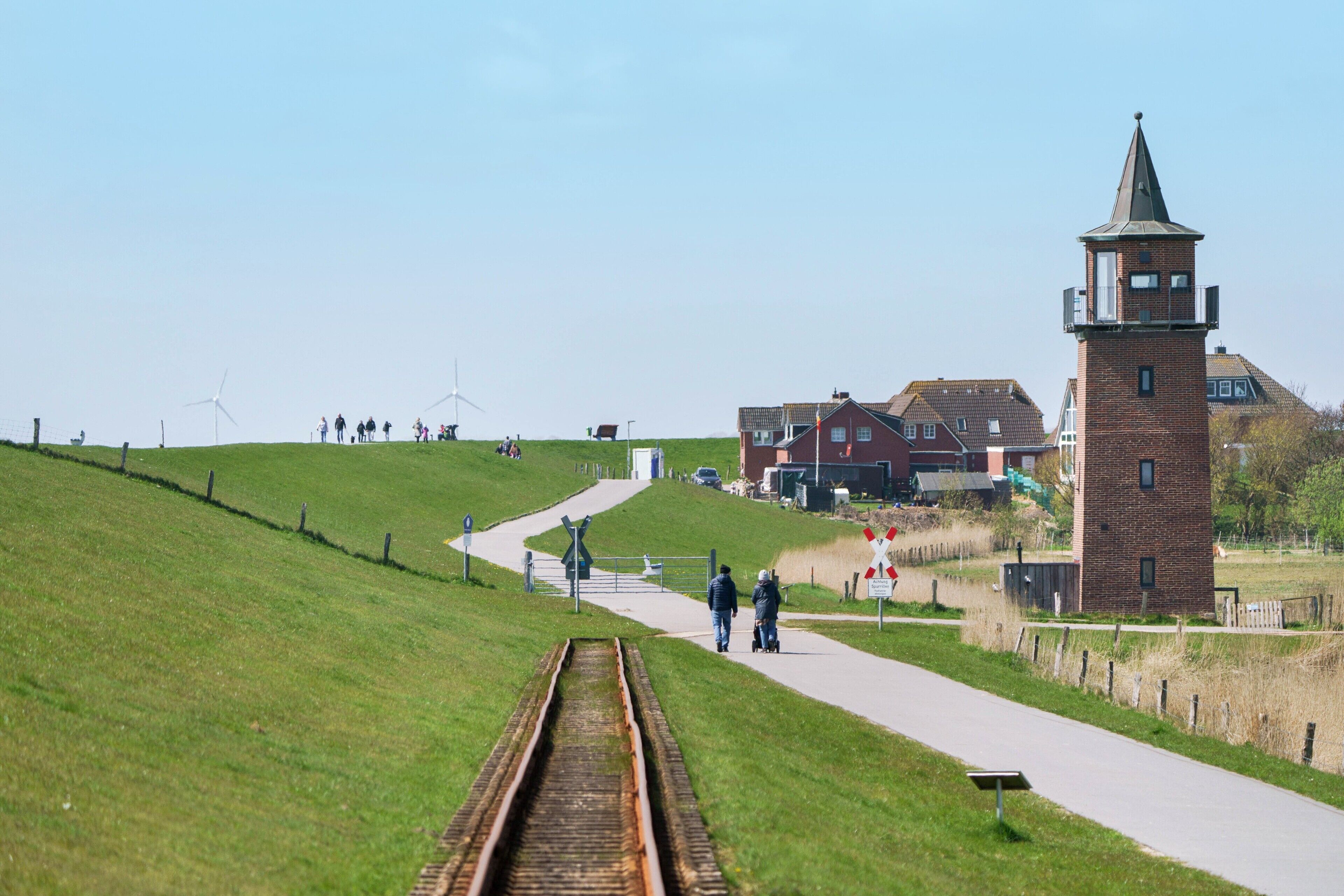 Gleise, ein Backsteinturm und ein Weg mit Spaziergängern.