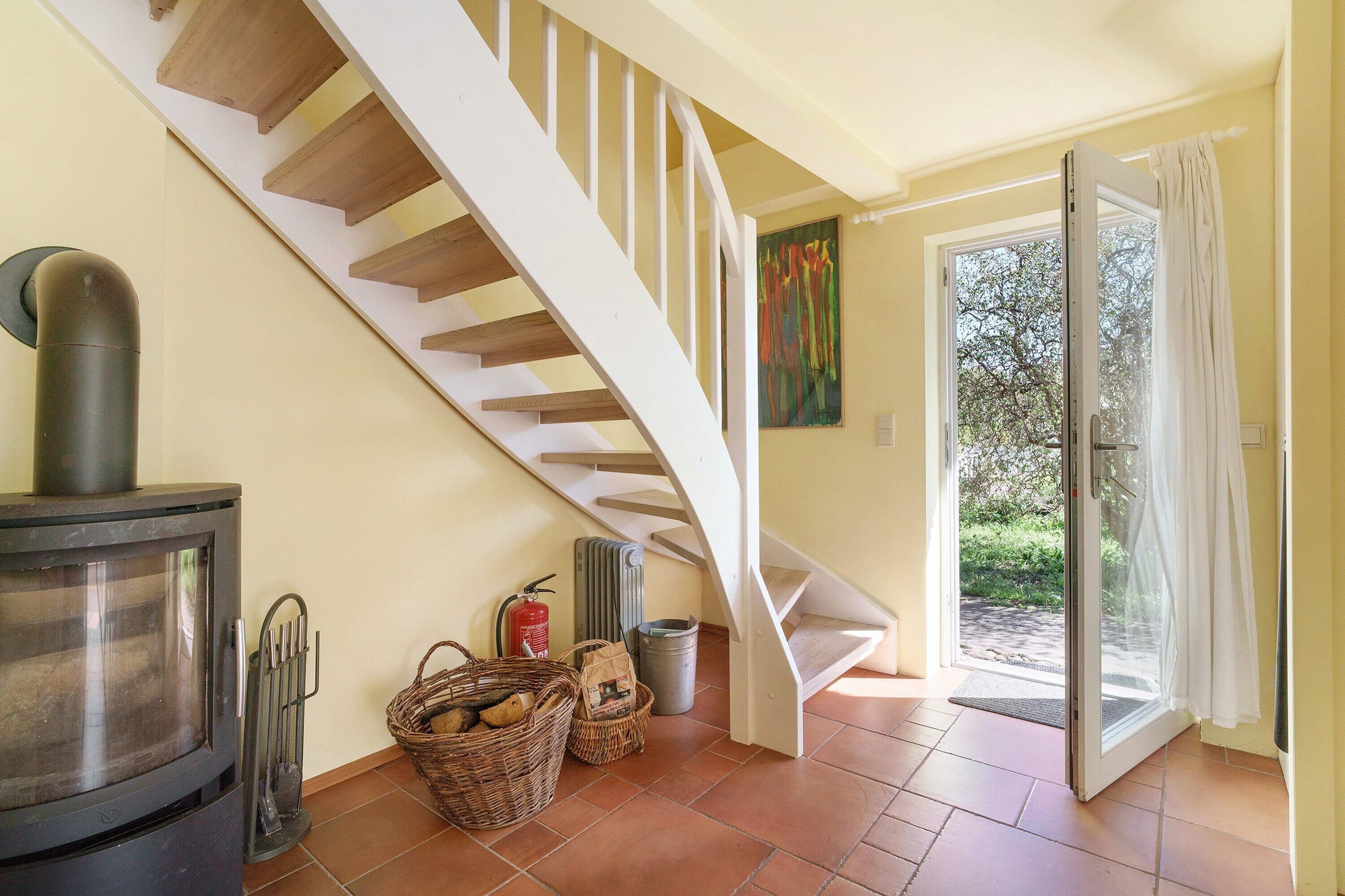 Un escalier avec une rampe blanche, un poêle à bois et une porte donnant sur un espace extérieur.