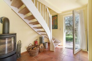 Una escalera con barandilla blanca, un estufa de leña y una puerta que da a un espacio exterior.