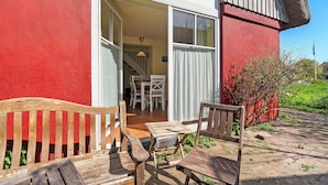 Un banco y una mesa de madera frente a un edificio con fachada roja y una escalera visible que conduce al interior.