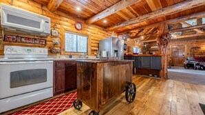 Eine rustikale Küchenzeile in einer Blockhütte mit Holzwänden, Holzbalkendecke, einer zentralen Kücheninsel auf Rädern, einer Mikrowelle, einem Kühlschrank und einem Herd.