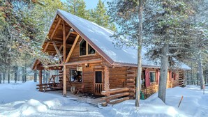 Eine Blockhütte mit großer Veranda, Holzfassade und verschneiter Umgebung.