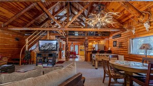 Ein Blockhaushaus-Interieur mit Holzboden, einem Fernseher, einem Esstisch und einem Kamin.