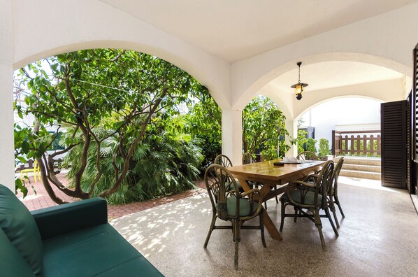 A dining area with a wooden table and chairs, surrounded by white arches and lush greenery. - Apartments Nada (Vodice)