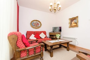 A living room with a red sofa, wooden armchairs, a wooden coffee table, a television, and a chandelier. - Apartments Nada (Vodice)