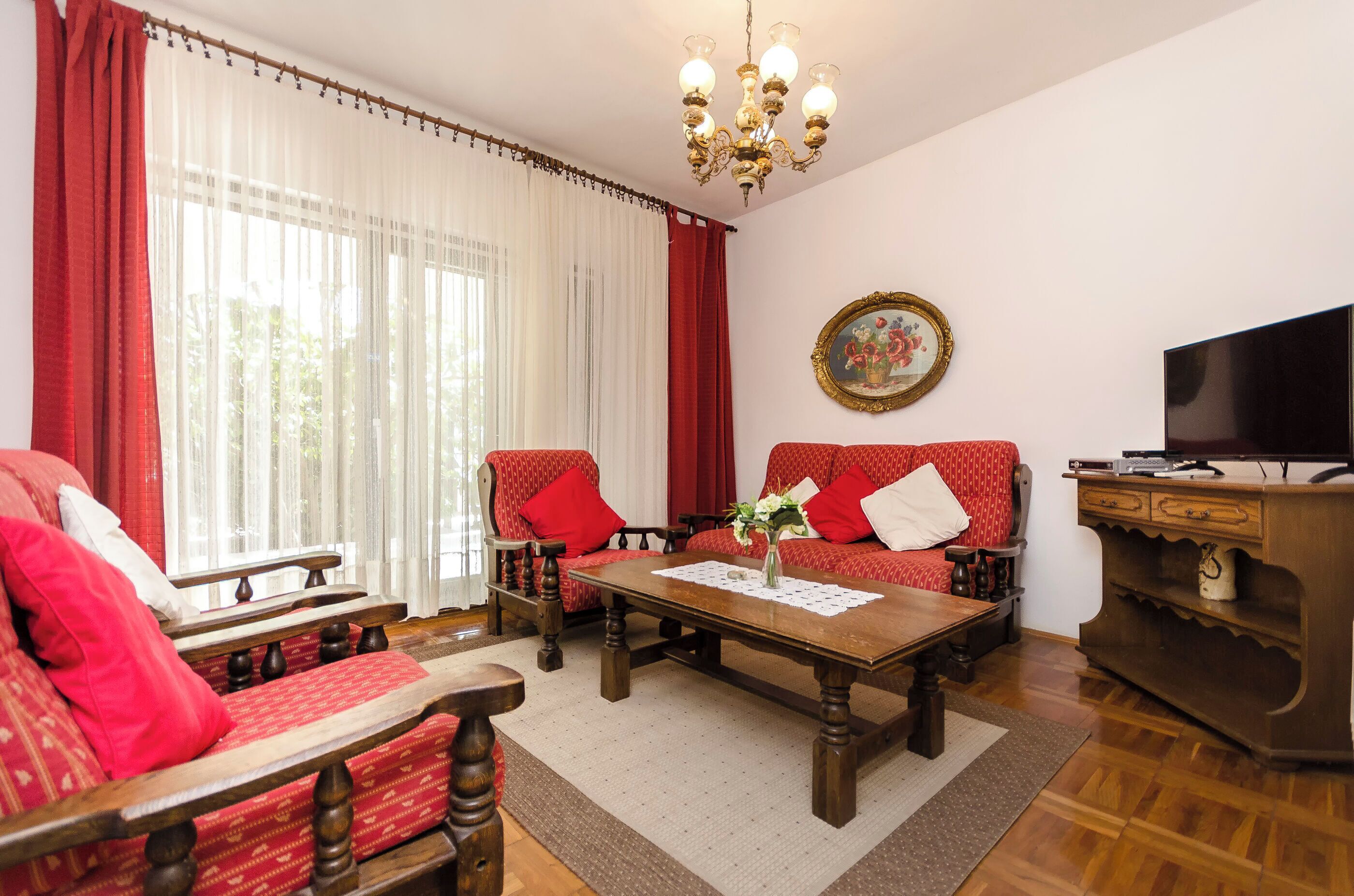 A living room with a wooden coffee table, red patterned sofa, and a television on a wooden cabinet.