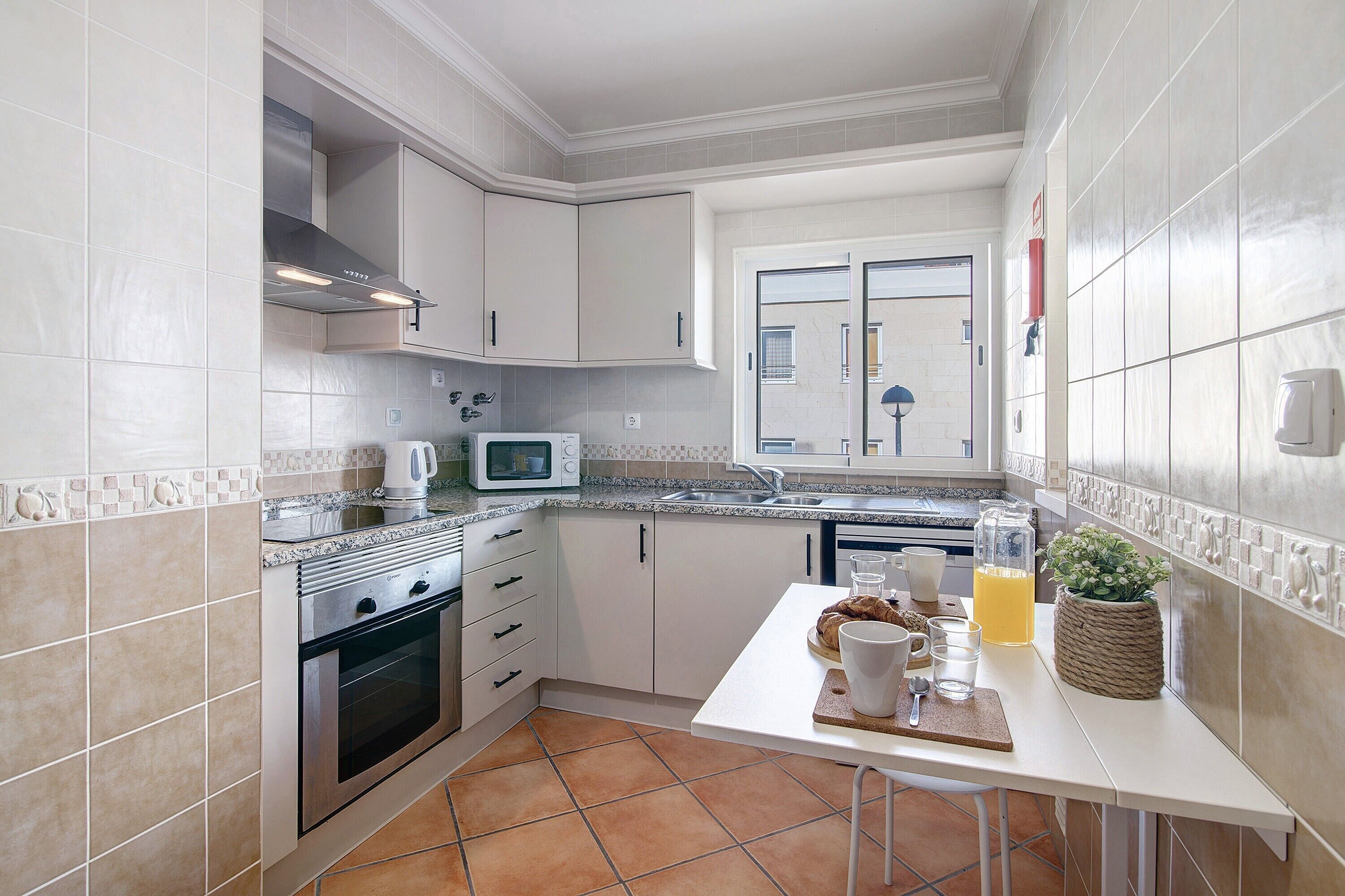 Una cocina con armarios blancos, microondas, estufa y ventana.