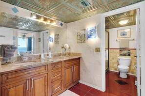 Un baño con tocador de mármol, armarios de madera, un espejo grande y un inodoro.