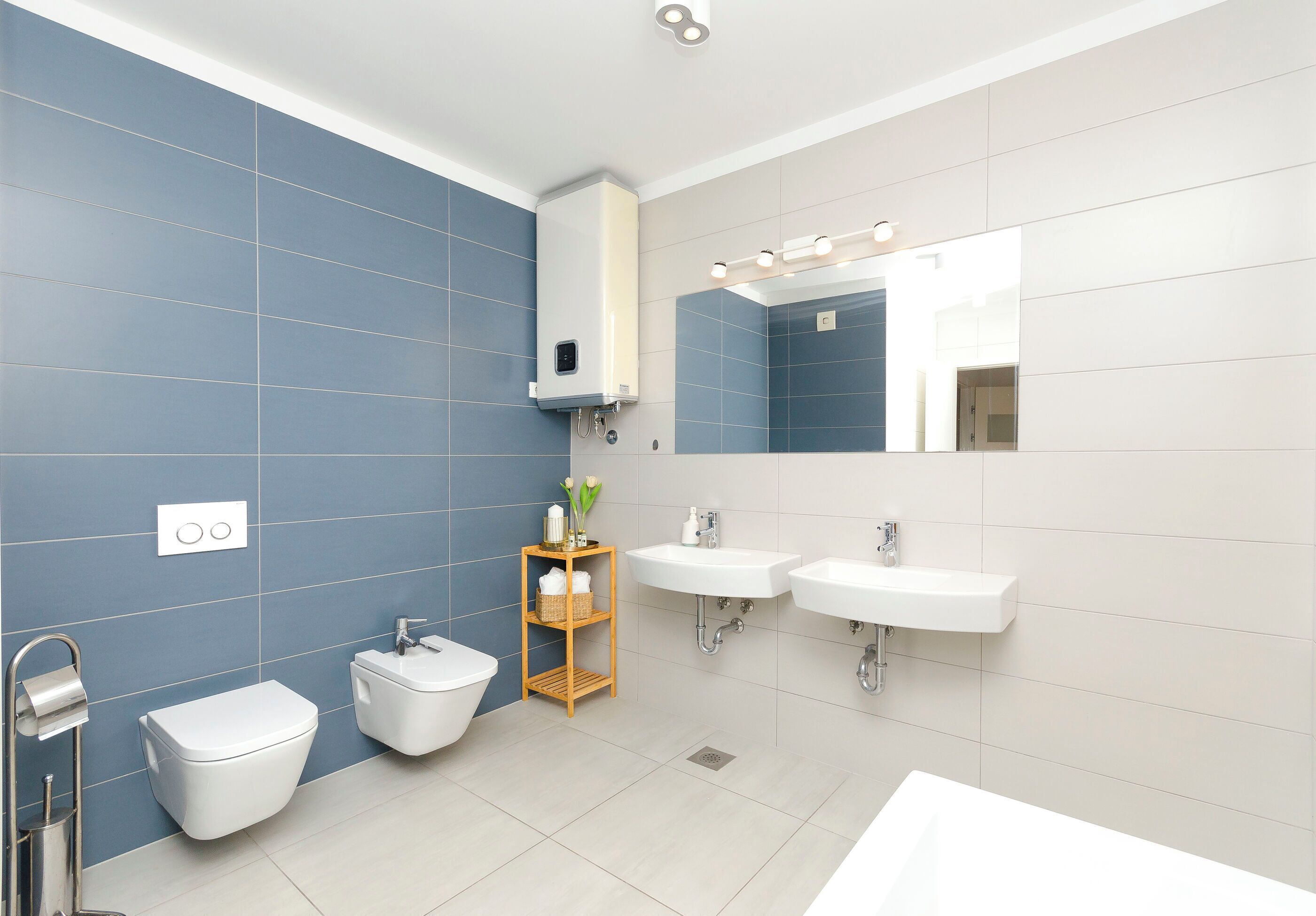 Une salle de bain moderne équipée d’un WC, d’un bidet, de deux lavabos et d’un miroir avec éclairage intégré.