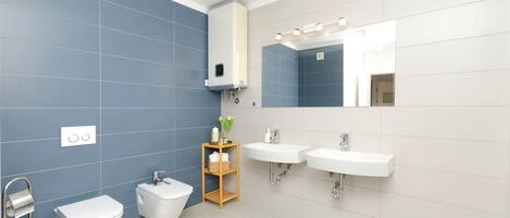 Une salle de bain moderne équipée d’un WC, d’un bidet, de deux lavabos et d’un miroir avec éclairage intégré.