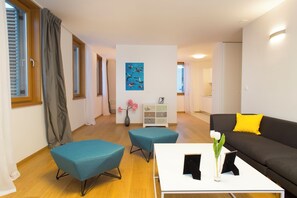 A modern living room with a sofa, two blue ottomans, a white coffee table, and a vase with flowers. - Apartment Toni Delux (Split)