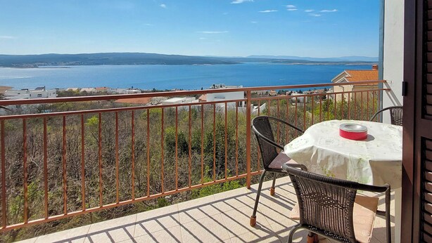Ein Balkon mit Tisch und Stühlen, der auf ein Gewässer und sanfte Hügel blickt.