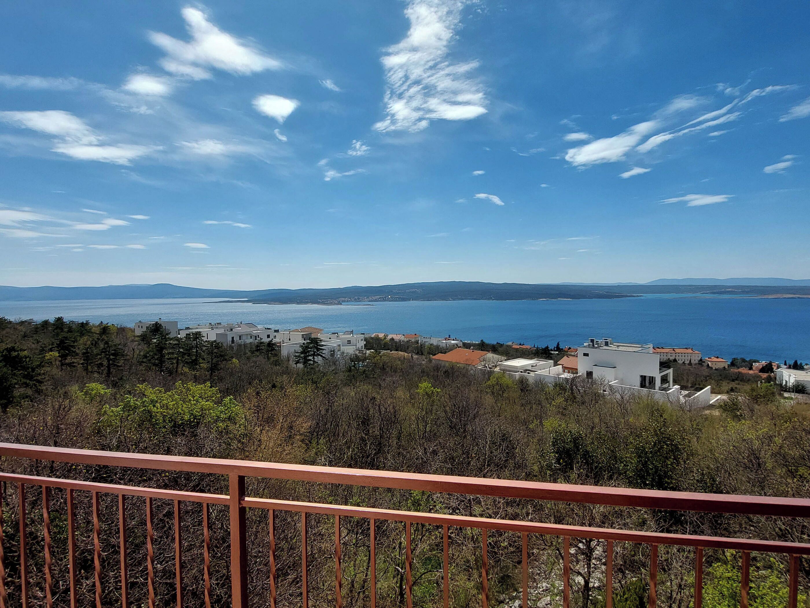 A coastal view with a clear sky, a body of water, and a forested area with buildings in the foreground.