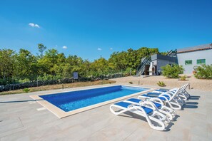 A swimming pool with lounge chairs, a stone wall, and a building with a red roof. - House Trget (Rasa)
