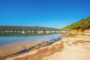 A coastal scene with clear water, boats, and a sandy beach. - House Trget (Rasa)