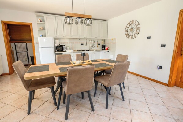A modern kitchen with white cabinets, a central island, and a dining area with six chairs. - House Trget (Rasa)