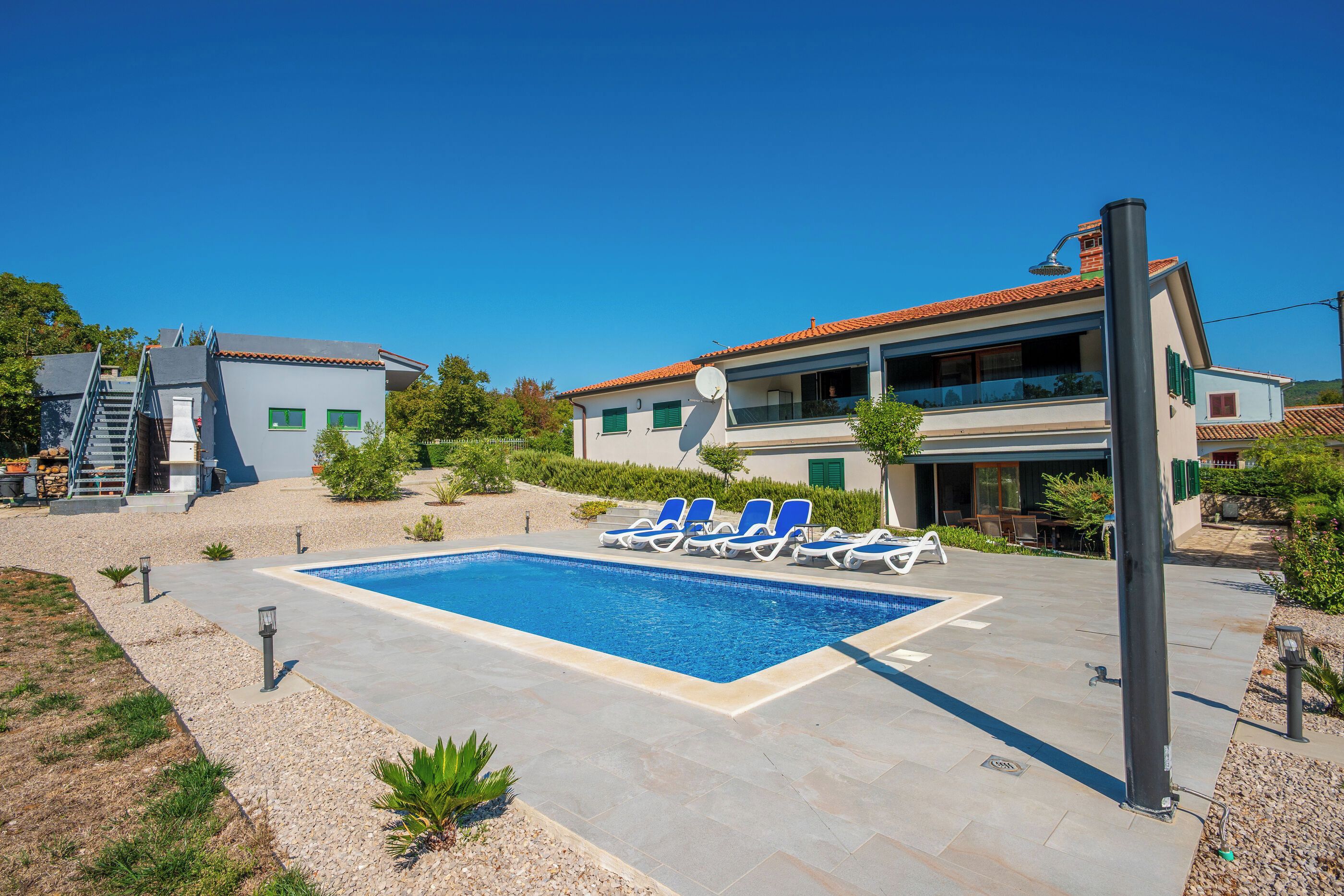A residential property with a swimming pool, lounge chairs, and a staircase leading to a second floor.