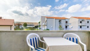 A terrace with two white plastic chairs with blue and white striped cushions, a white table, and a view of buildings with red-tiled roofs. - Apartments Josip S (Lopar)