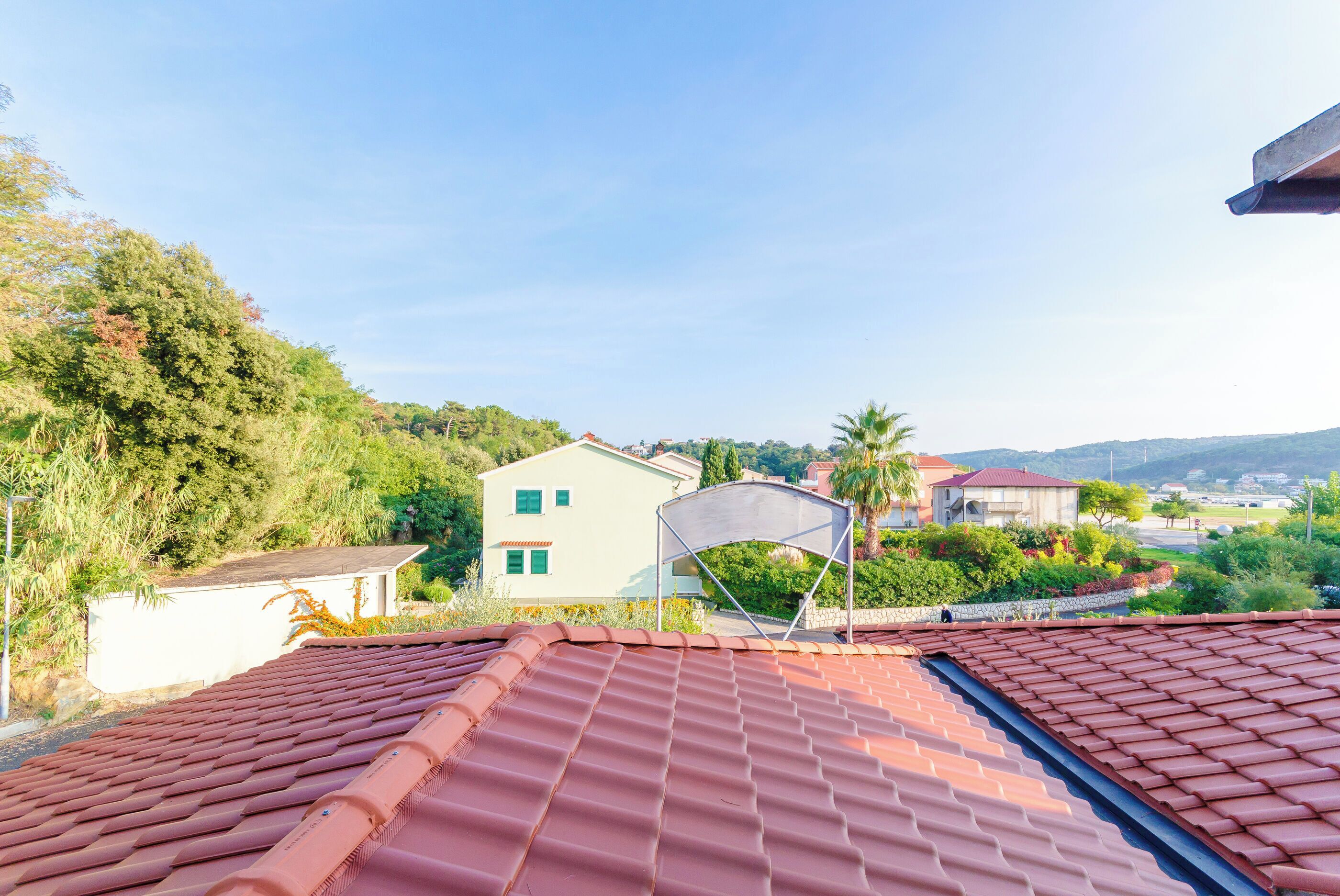 A red-tiled roof with a view of a white building and surrounding greenery.