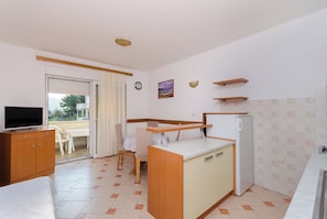 A compact hotel room with a kitchenette, a bed, a TV, a dining area with a table and chairs, and a view through the glass door. - Apartments Josip S (Lopar)