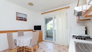 A compact kitchen with a gas stove, a dining table with chairs, a television, and a sliding glass door leading to a balcony. - Apartments Josip S (Lopar)