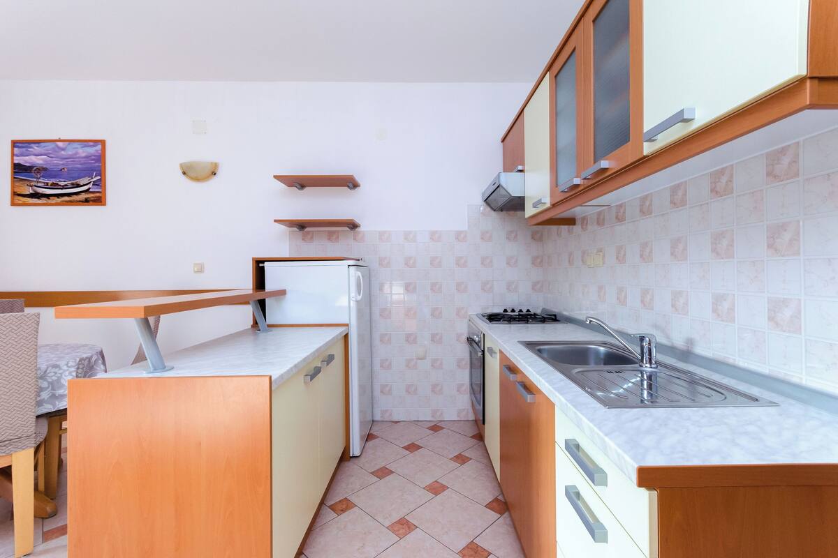 A compact kitchen with a refrigerator, stove, sink, and wooden cabinets.