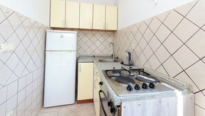 Egy praktikus, kis méretű konyha, amelyben hűtőszekrény, tűzhely, mosogató és világos színű szekrények találhatók.