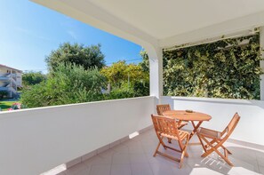 Ein Balkon mit weißer Wand, Holzmöbeln und Blick auf Grünflächen und Gebäude.