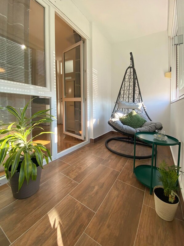 A cozy balcony with a hanging chair, a small table, and potted plants. - Apartment Wolfie (Sibenik)