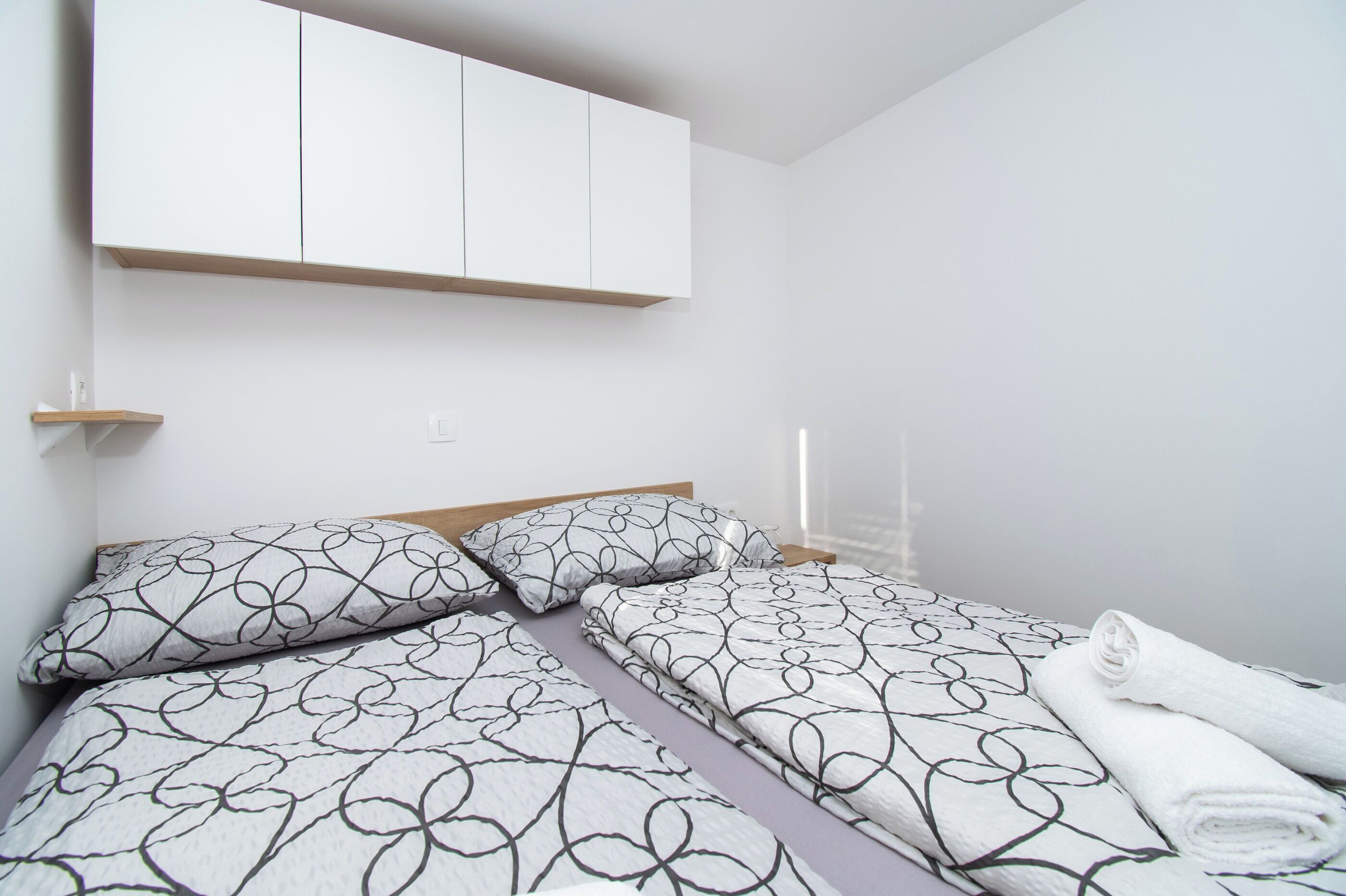 A neatly made bed with patterned bedding, a wooden headboard, and a white wardrobe above.