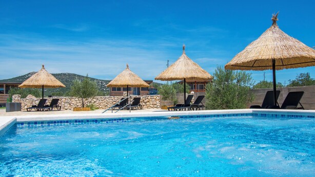 A swimming pool with lounge chairs and thatched umbrellas. - Mobile Home Banovi Dvori (Tisno)