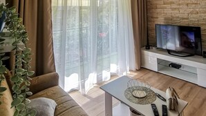 A living room with a sofa, a coffee table, a TV on a stand, and a stone wall. - House Neda (Marina)