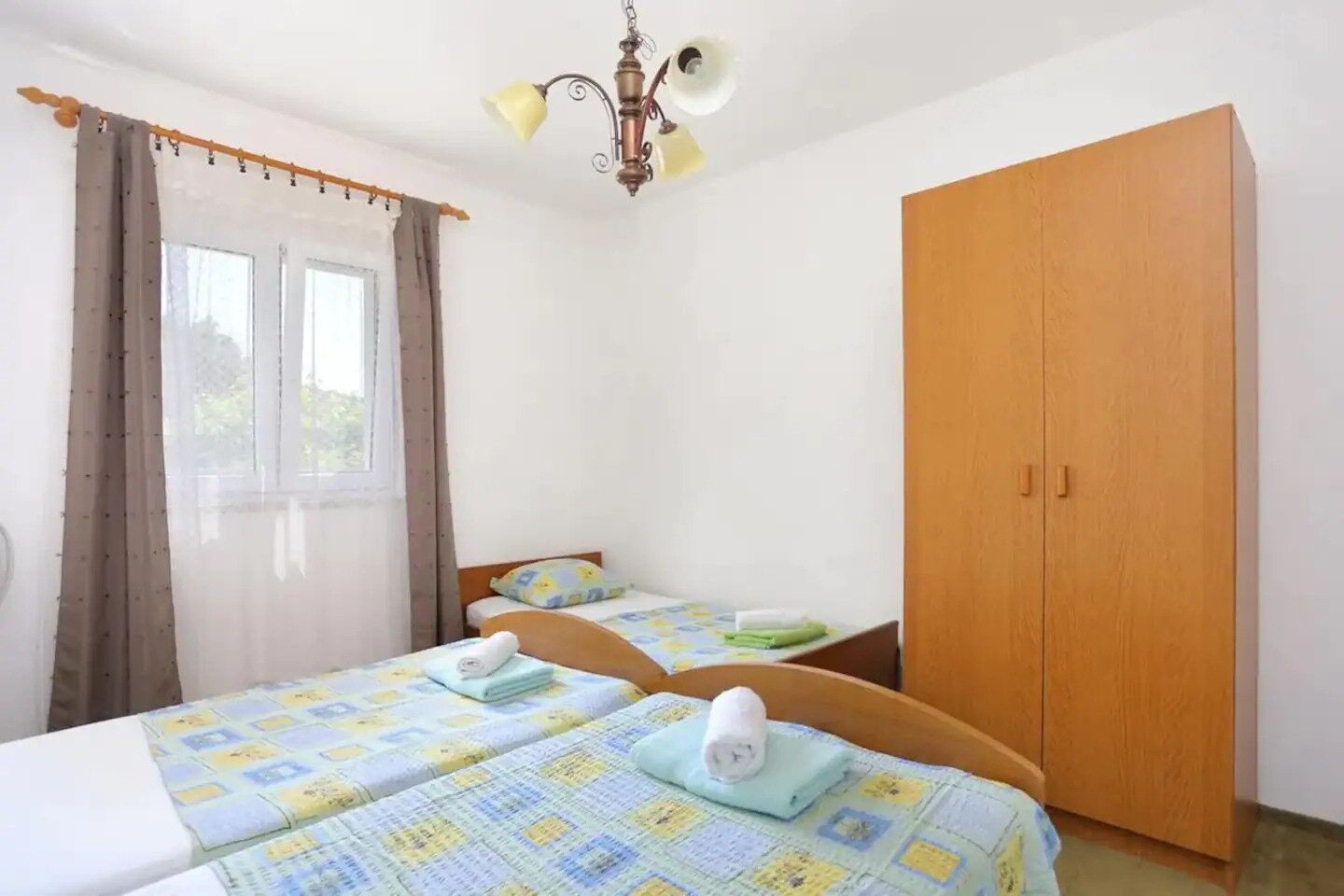 Ein Schlafzimmer mit zwei Betten, einem Holzschrank, einem Fenster mit Vorhängen und einer Deckenleuchte.
