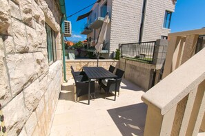 Ένας εξωτερικός χώρος με τραπέζι και καρέκλες, έναν τοίχο από πέτρα και θέα σε ένα κτίριο με μπαλκόνια.