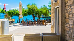An outdoor seating area with tables and chairs, overlooking a body of water. - Apartment Centar (Postira)
