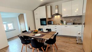 Una cocina moderna con armarios blancos, una mesa de comedor de madera con sillas negras y una pequeña isla con microondas y hervidor.