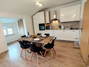Eine moderne Küche mit weißen Schränken, einem Holzespeisetisch mit schwarzen Stühlen und einer kleinen Kochinsel mit Mikrowelle und Wasserkocher.
