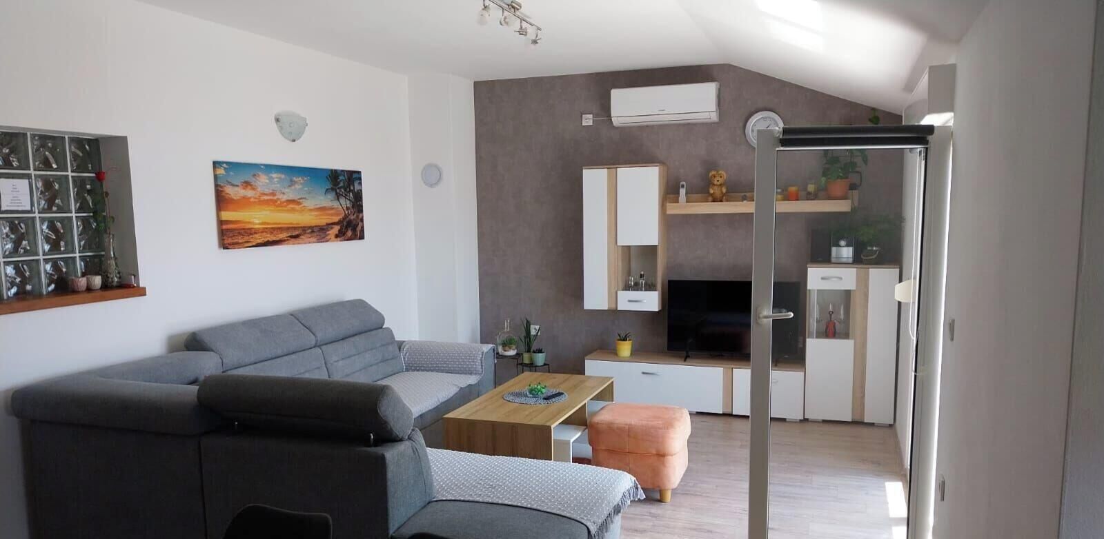 Un salon moderne avec un canapé gris, une table basse en bois et un tableau représentant un coucher de soleil.