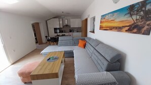 Una sala de estar moderna con un sofá seccional gris, una mesa de centro de madera y una cocina al fondo.
