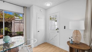 Ein helles, weißes Interieur mit einem Glastisch, weißen Stühlen, einem Holzboden und einer Tür mit Fenster.
